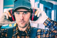Factory Worker Wearing Hearing Protectors and Protective Goggles.